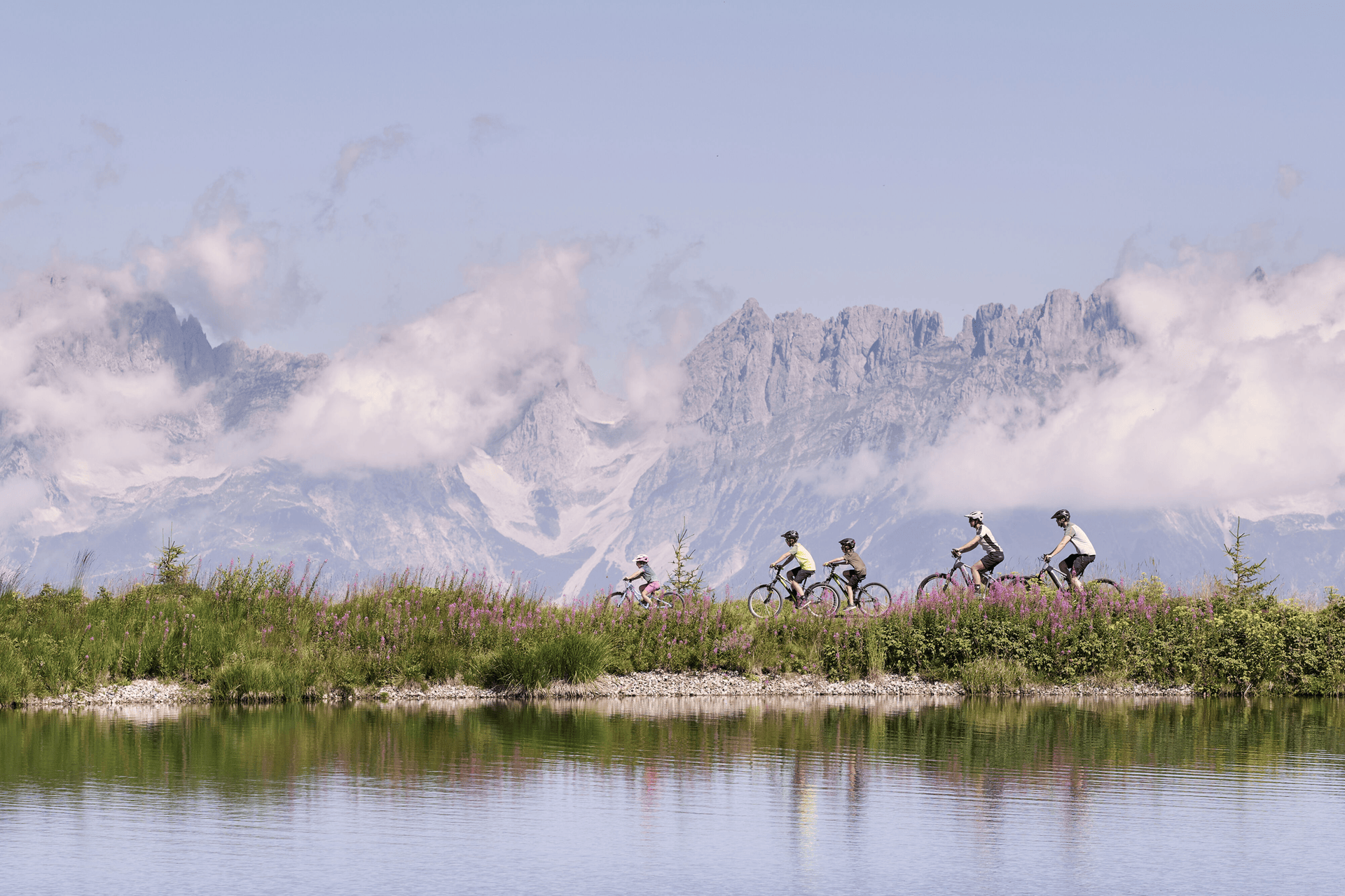 Drei Radfahrer fahren auf einem kurvenreichen Weg durch eine üppig grüne Berglandschaft bergauf und vermitteln unter einem teilweise bewölkten Himmel ein Gefühl von Abenteuer und Entschlossenheit.