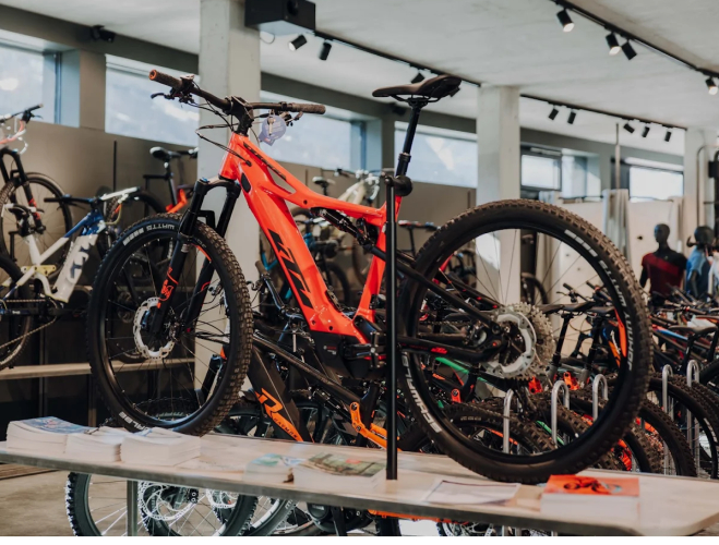 Ein leuchtend orangefarbenes Mountainbike, ausgestellt in einem modernen Fahrradgeschäft, umgeben von anderen Fahrrädern. Das Geschäft hat einen hellen, industriellen Stil.